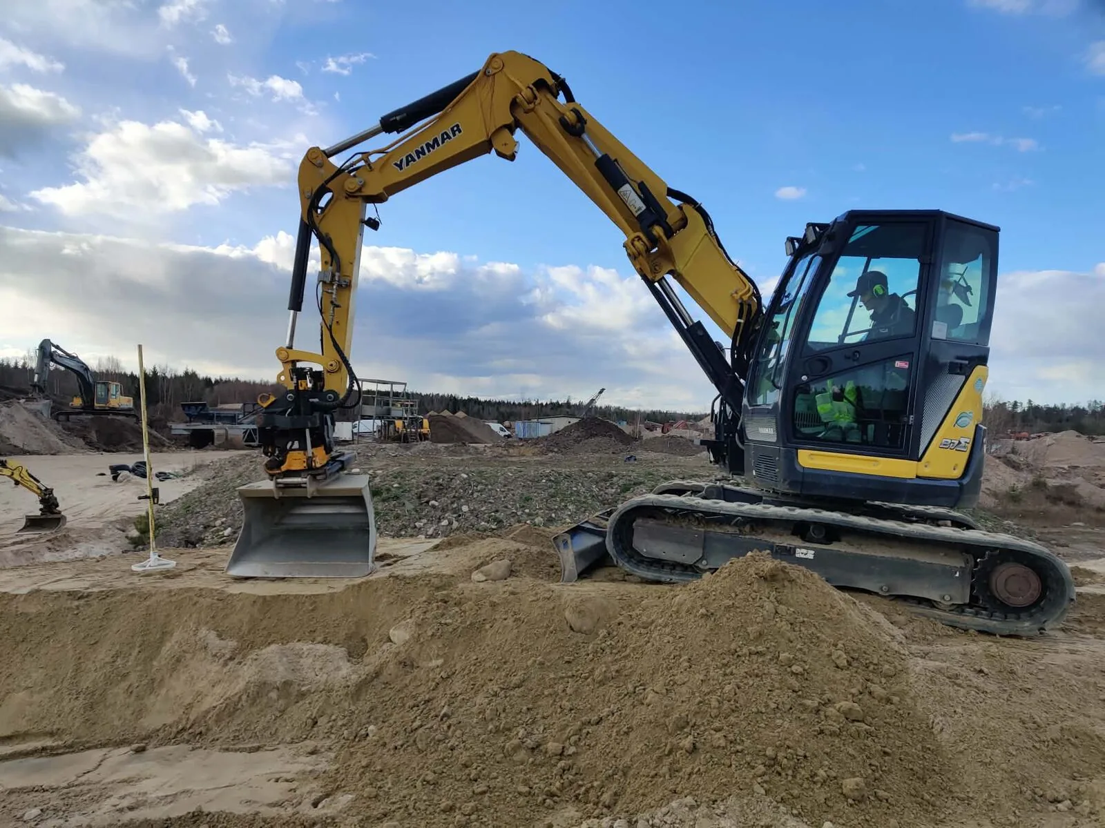 Grävmaskin med tiltrotator vid en sandhög